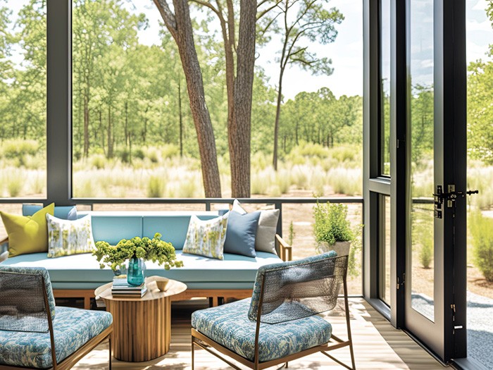 Sunroom featuring oak wood patio furniture with light blue and light green cushions overlooking the green forest.